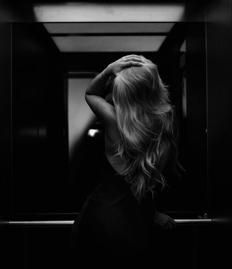 A companion alone in a mirrored lift, her face turned away from the camera.